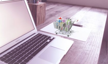 eCommerce and Merchandising Laptop next to mini shopping trolley containing gifts