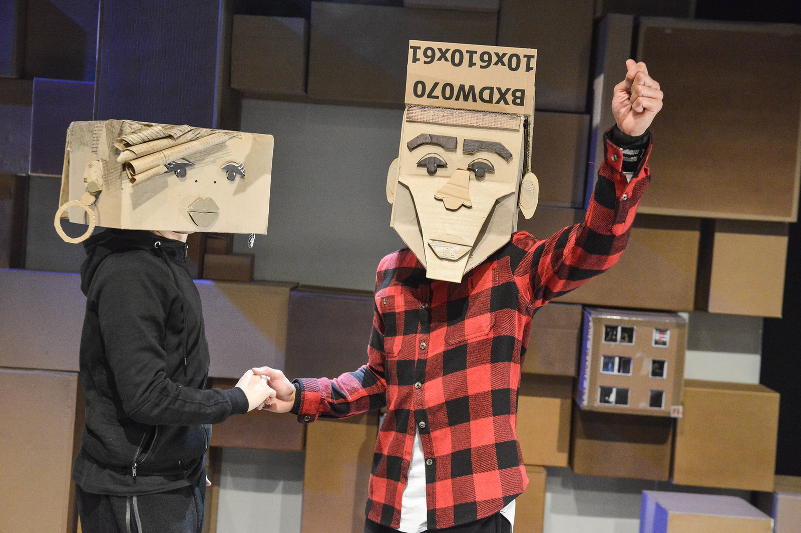 Two people wearing cardboard masks shake hands