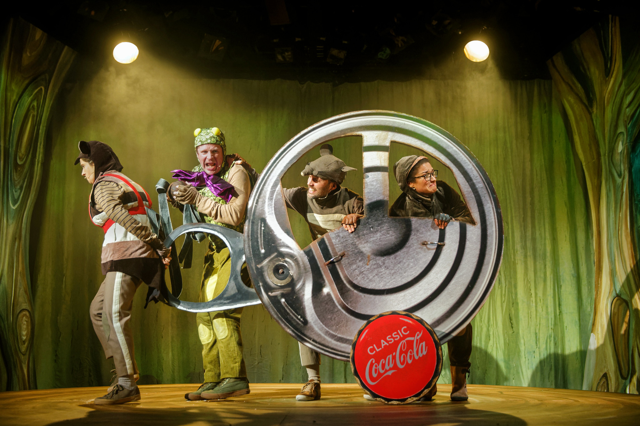 Image of actors on stage inside a large soft drink can lid