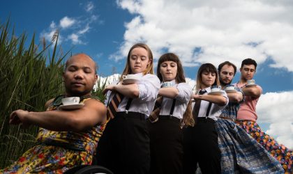 Row of people balancing tea cups on their arms