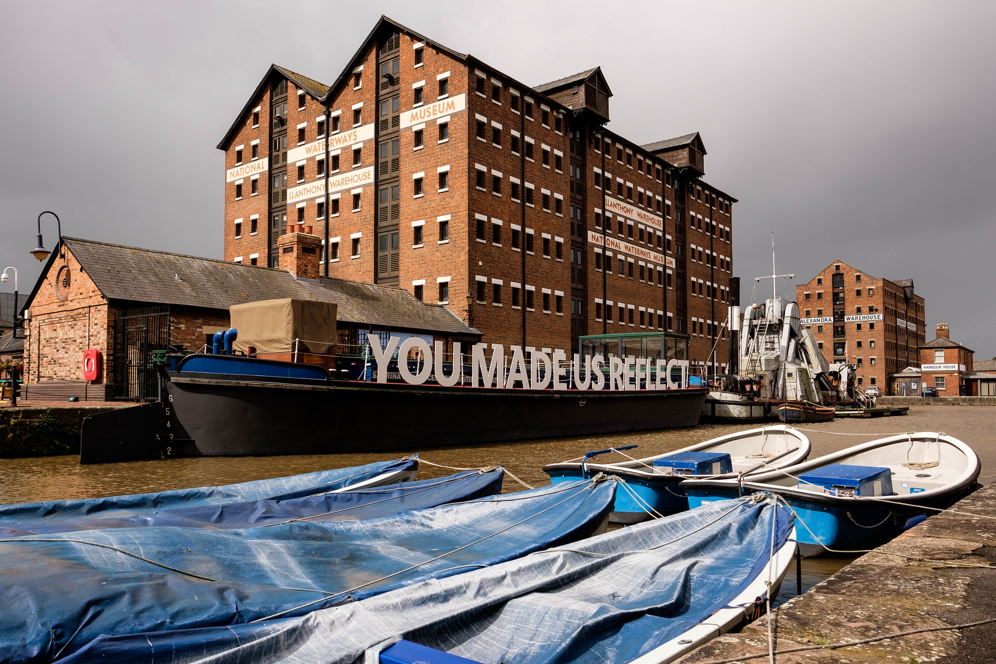 View of an old factory building with a river and boats in the foreground. One boat has the words 'you made us reflect'.