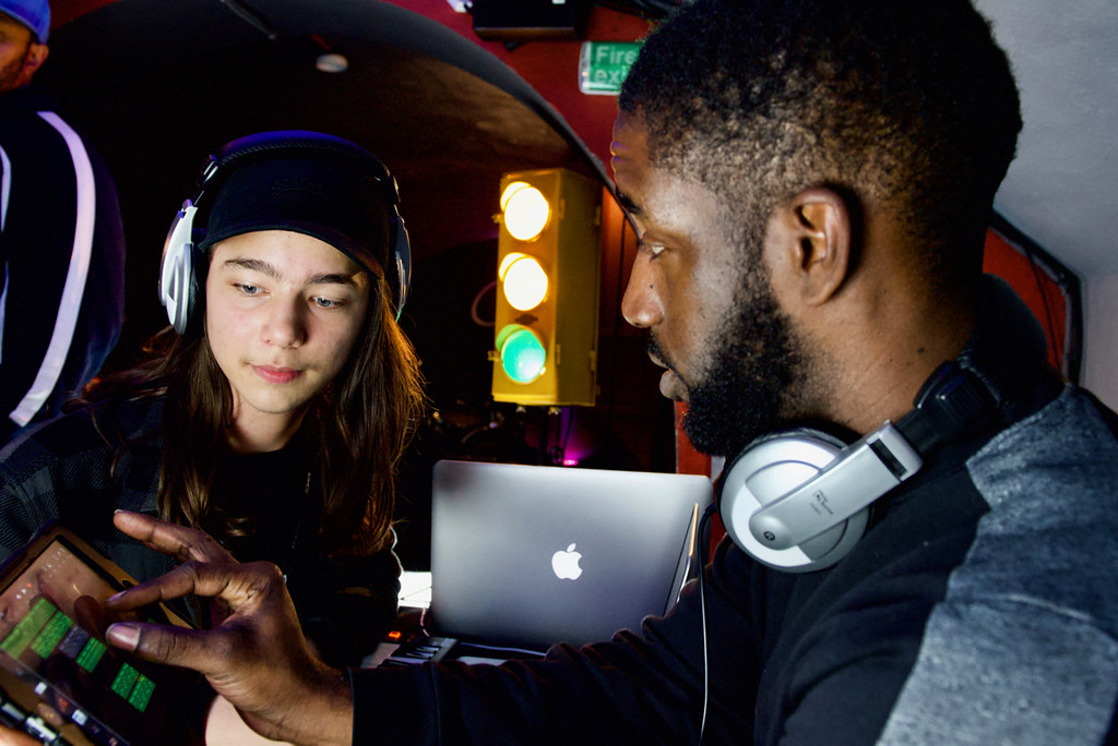 NFT Image of two young people looking at a tablet screen, both wearing headphones.