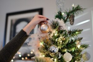 Image of a hand placing a gold bauble on to a decorated Christmas tree