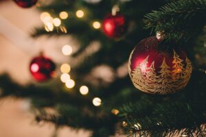 Close up image of a red bauble hanging on a Christmas tree with blurred out fairy lights.