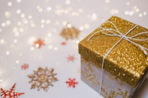 Image of a gift wrapped box on a table. The box lid is sparkly gold and there are sparkly snowflakes on the table.