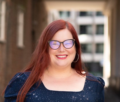 Tech Champion Nicola Barratt, with red hair and wearing glasses and a blue dress.