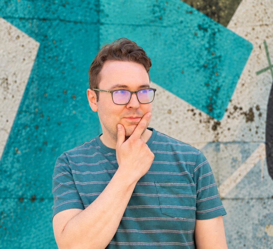 Jack wearing glasses and a green striped top with hand on face looking bemused. Against a green and whit abstract background.