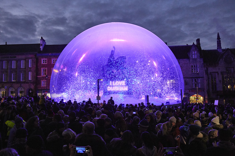 Image of large snow globe like dome lit up with dark sky and group of people watching
