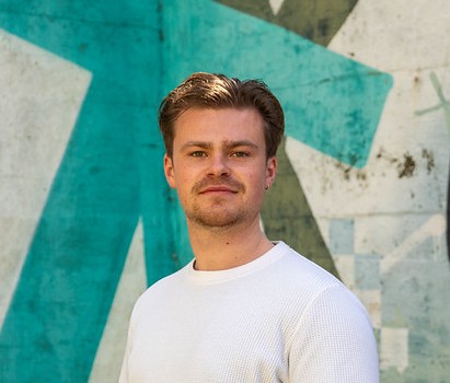 Mike wearing white top and smiling against an abstract green and white background.