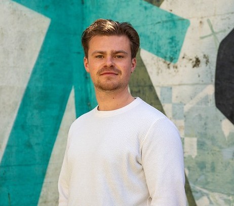 Mike wearing a white top against a green and white painted wall.