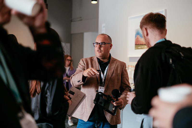 A person holding a microphone surrounded by guests in an art gallery