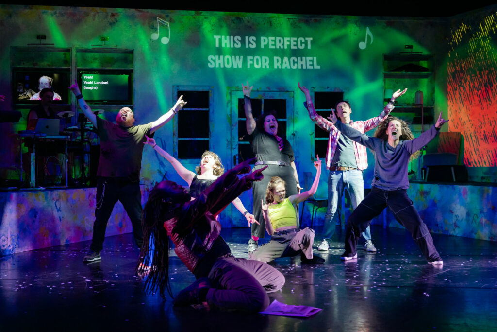 A group f performers on a stage expressing joy and happiness through different poses. The background is colourful and full of green light.