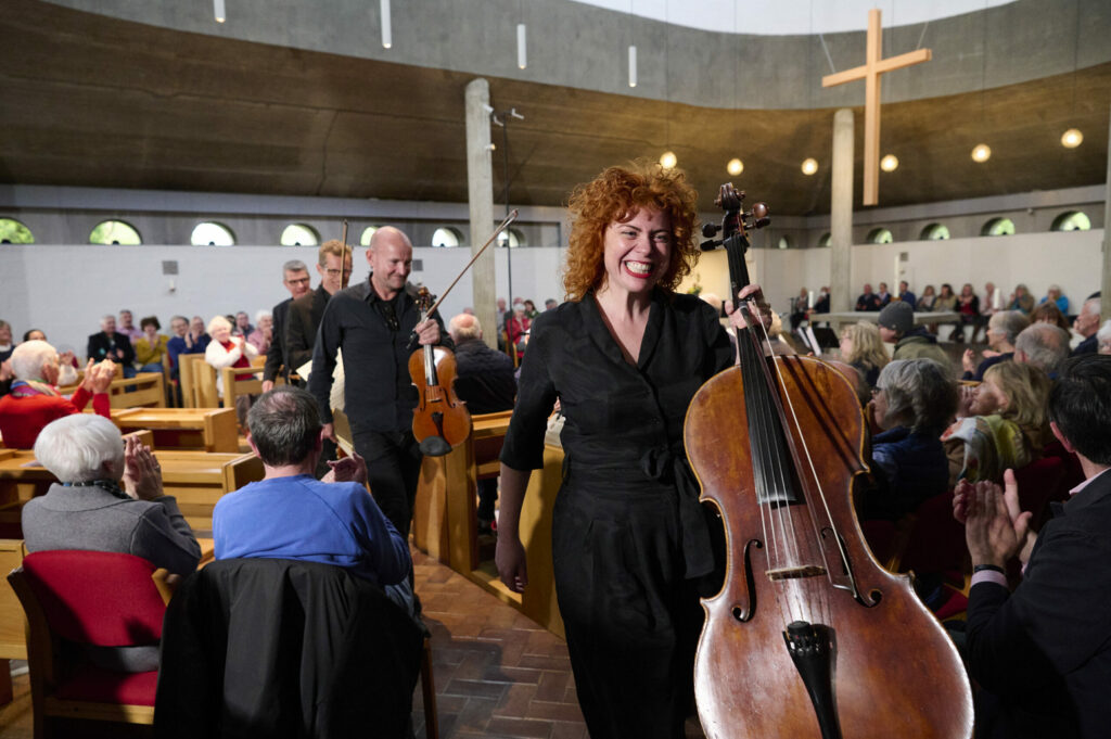 Musicians walking through audience members in a busy music venue, holding their instruments.