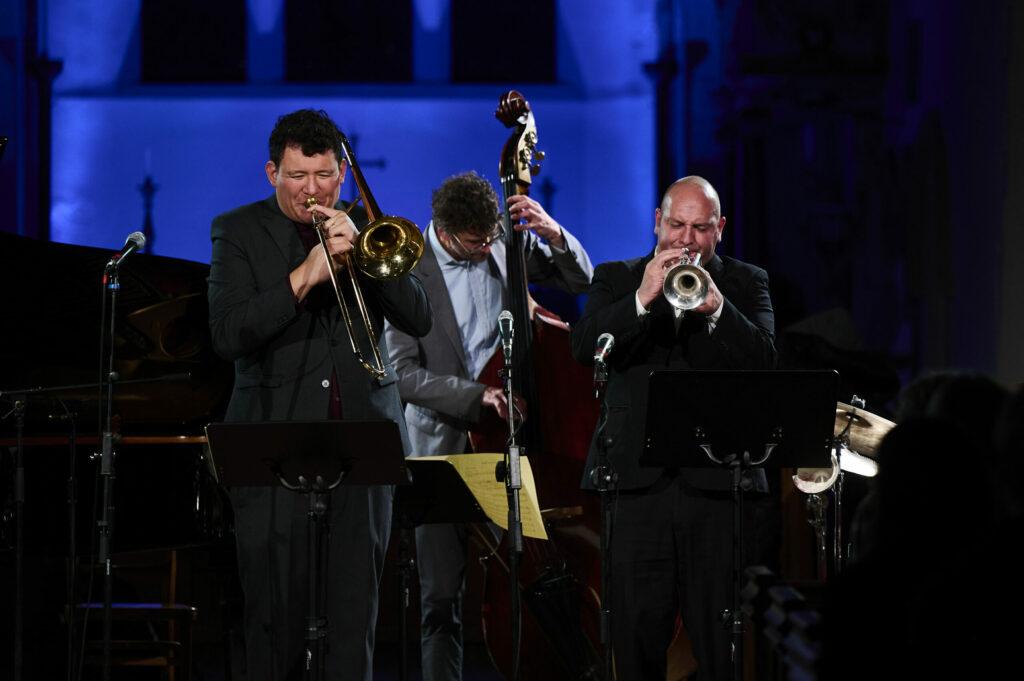 Three men performing on stage with brass instruments.