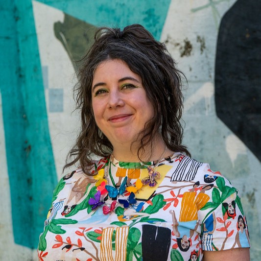 Alison wearing colourful top and smiling against a patterned wall background.