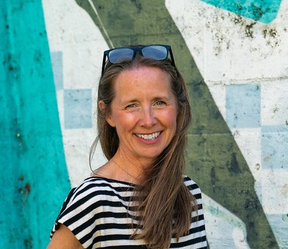 Charlotte smiling and wearing a striped top, against a green patterned wall background.