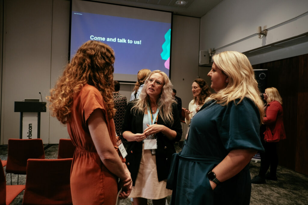 Three women stand talking at a Digital Culture Network event.